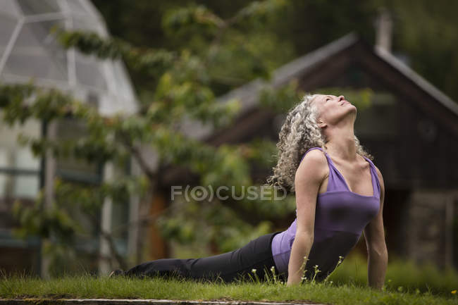 Mature woman practicing yoga upward dog in eco lodge garden — Stock Photo