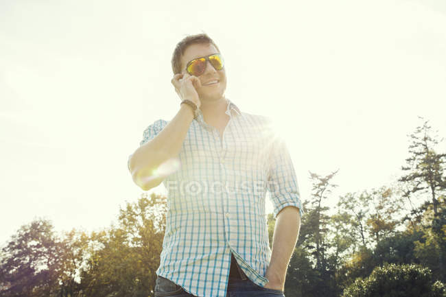 Молодий чоловік спілкується на смартфоні в парку під підсвічуванням — стокове фото