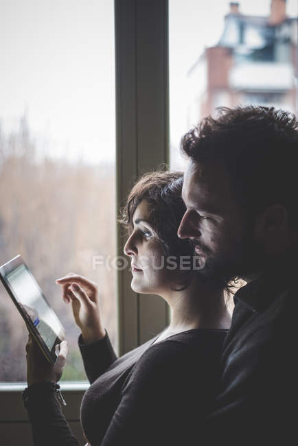 Пара стоїть біля вікна, використовуючи цифровий планшет — стокове фото