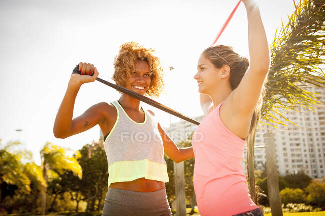 Two young female friends training with exercise bands in park — Stock Photo