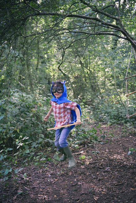 Boy dressed in cape running in forest — Stock Photo