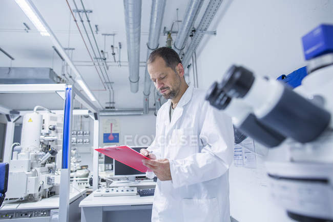 Lab assistant checking research detail on clipboard — Stock Photo