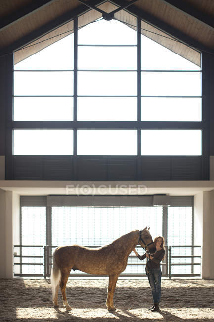 Jovem mulher stablehand pé com cavalo palomino — Fotografia de Stock