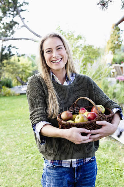 Femme adulte moyenne tenant panier de pommes, portrait — Photo de stock