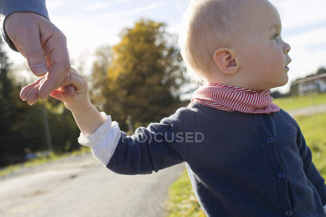 Baby girl toddling on rural road holding fathers hand — Stock Photo