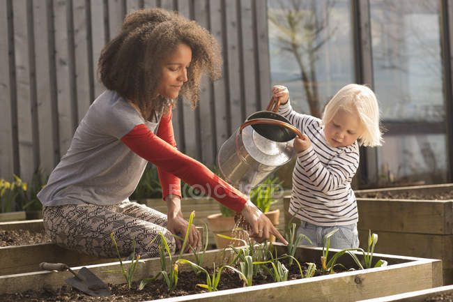 Mulher adulta média ajudando filho plantas de água na cama levantada — Fotografia de Stock