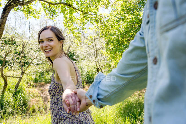 Mujer joven guiando a un joven a través del bosque, cogido de la mano - foto de stock