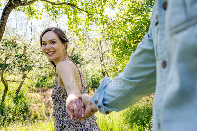 Jeune femme conduisant jeune homme à travers la forêt, tenant la main — Photo de stock