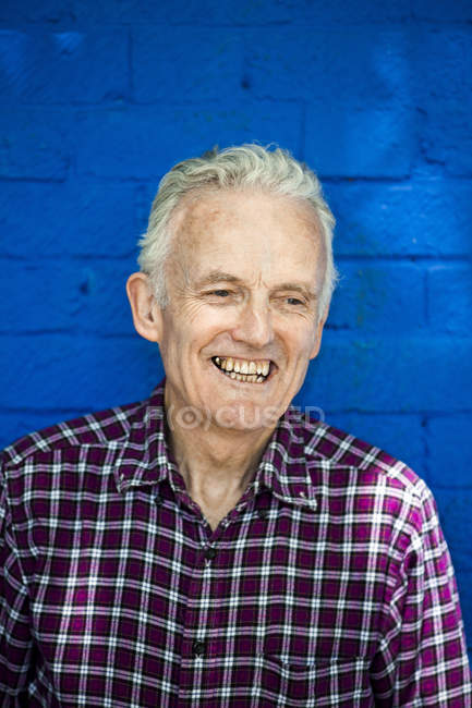 Porträt eines glücklichen älteren Mannes, blaue Backsteinwand im Hintergrund — Stockfoto