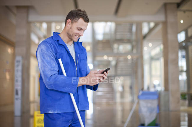 Мужчина чистильщик смс на смартфоне в офисном атриуме — стоковое фото
