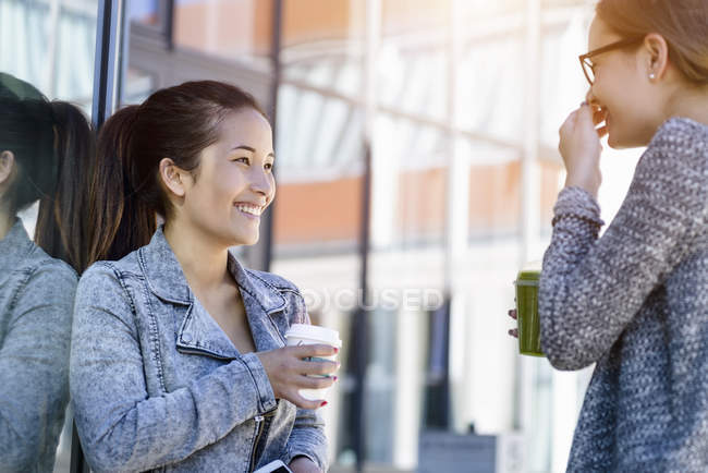 Две молодые женщины с кофе на вынос смеются — стоковое фото