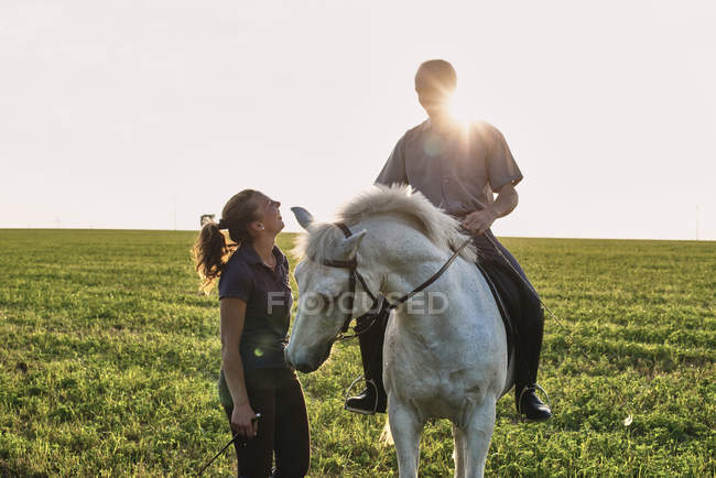 Woman chatting with man riding grey horse in field — Stock Photo