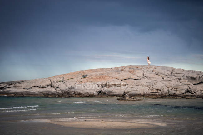 Vista lejana de una joven paseando por la formación rocosa en la costa, Costa Rei, Cerdeña, Italia - foto de stock
