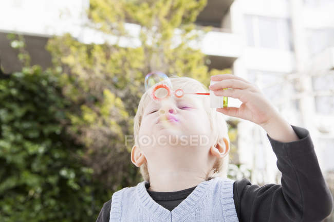 Маленький хлопчик дме бульбашки в саду — стокове фото