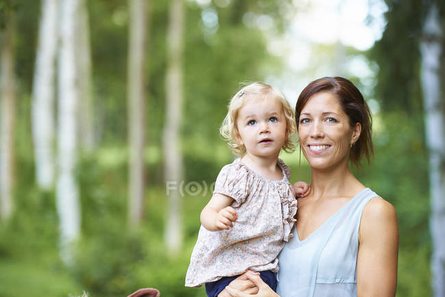 Portrait mid adult woman and toddler daughter in garden — Stock Photo