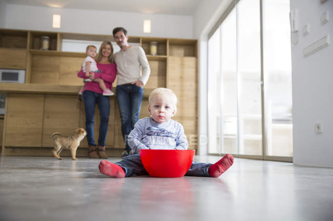 Familia viendo niño varón con cuenco en el piso del comedor - foto de stock