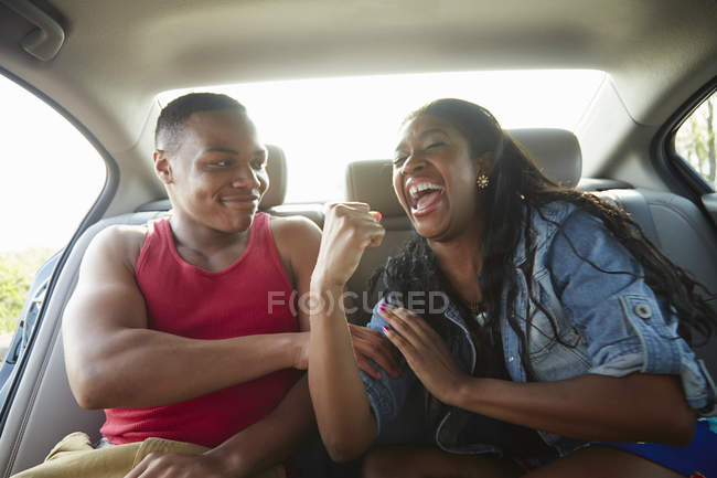 Jovem casal no carro rindo, mulher flexionando músculos — Fotografia de Stock