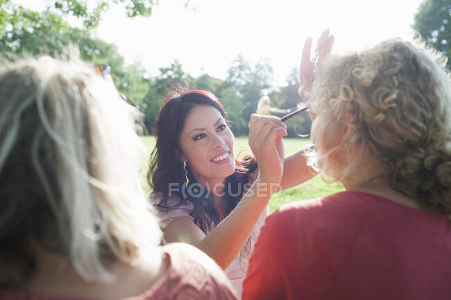 Feminino adultos amigos aplicando maquiagem no pôr do sol parque festa — Fotografia de Stock