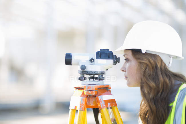 Agrimensora femenina mirando a través del nivel en el sitio de construcción - foto de stock