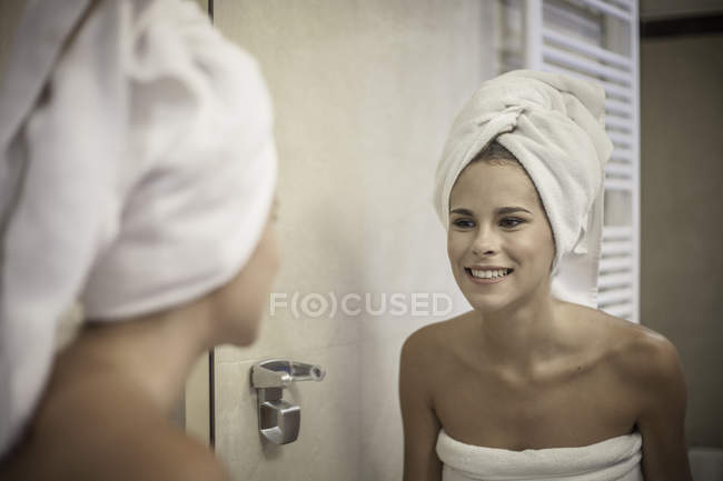 Young woman wearing towel on head looking at reflection in mirror — Stock Photo
