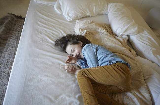Хихикающая молодая девушка свернувшаяся на кровати — стоковое фото