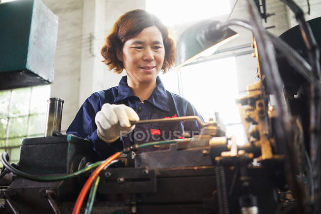Mature female worker using equipment in crane manufacturing facility, China — Stock Photo