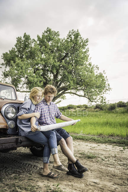 Chica adolescente y novio leyendo mapa en el parachoques del jeep - foto de stock
