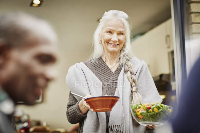Mujer mayor llevando tazones de ensalada afuera - foto de stock