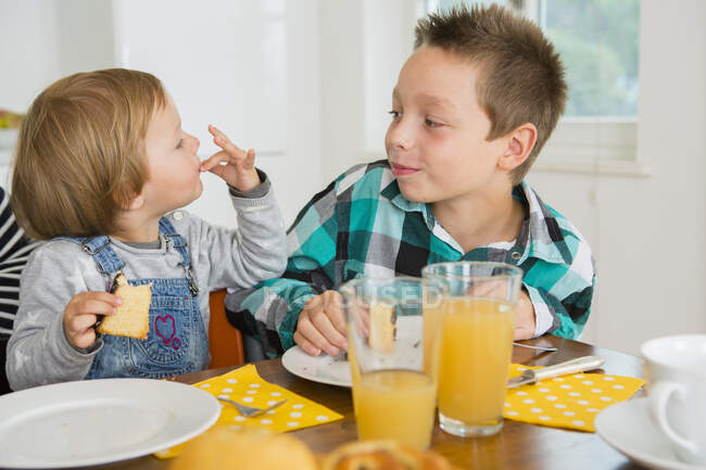 Cute female toddler licking fingers at kitchen table — Stock Photo