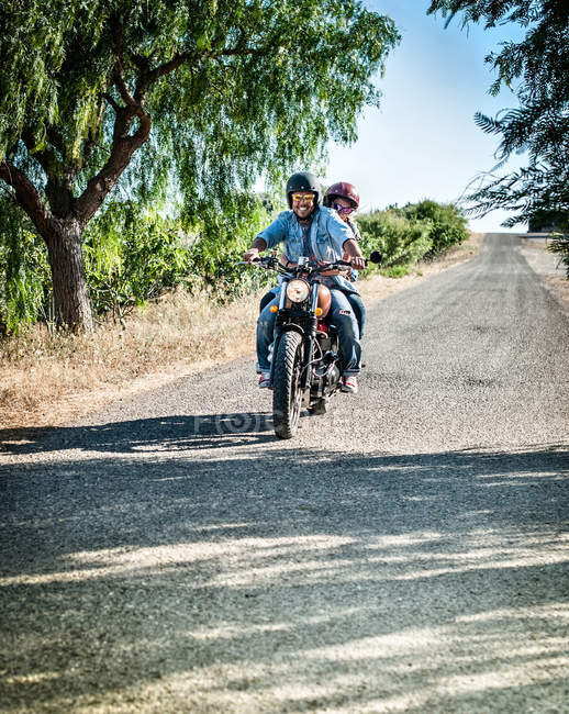 Mid adult couple riding motorcycle on rural road, Cagliari, Sardegna, Italia — Foto stock