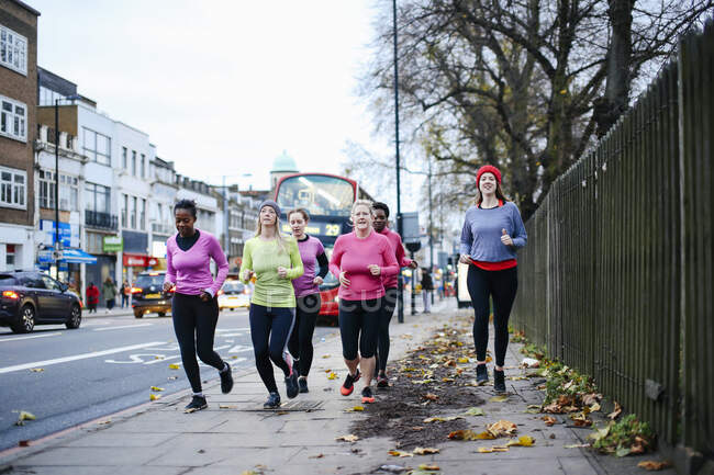 Five female runners running on city sidewalk — Stock Photo
