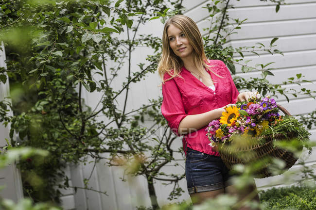 Young woman with basket of flowers in garden — Stock Photo