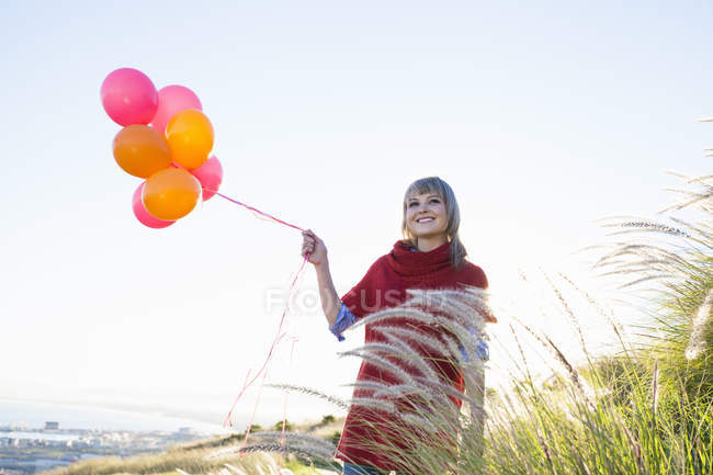 Giovane donna sulla collina erbosa con un mucchio di palloncini — Foto stock