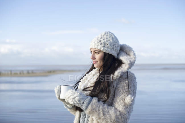 Young woman holding coffee on beach, Brean Sands, Somerset, England — Stock Photo