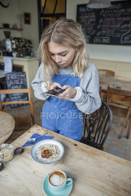 Mujer joven en la cafetería, utilizando el teléfono inteligente - foto de stock