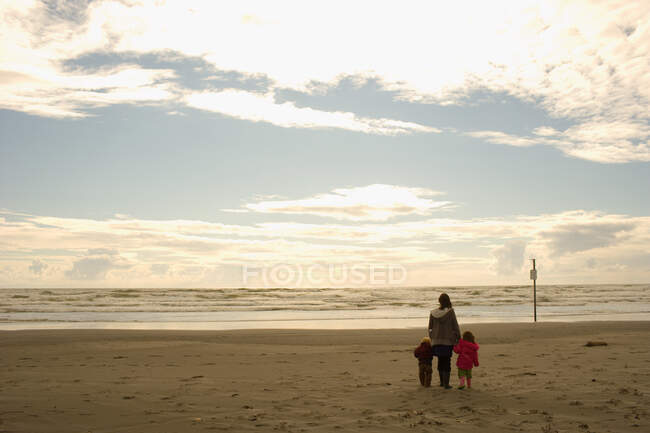 Mãe com filho e filha de mãos dadas na praia de areia — Fotografia de Stock