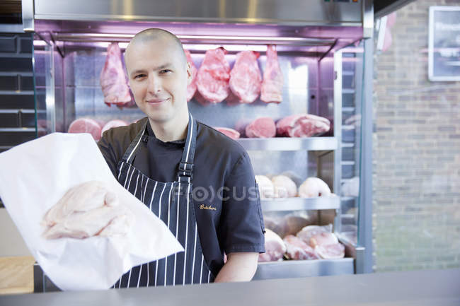 Retrato del carnicero sosteniendo pechuga de pollo en carnicería - foto de stock