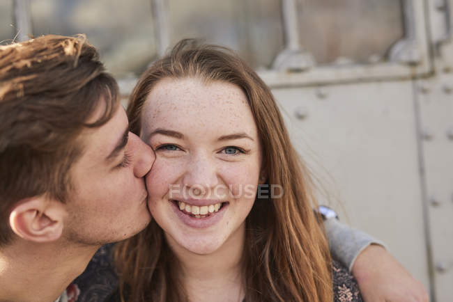 Hombre joven besando a mujer joven en la mejilla, Bristol, Reino Unido - foto de stock
