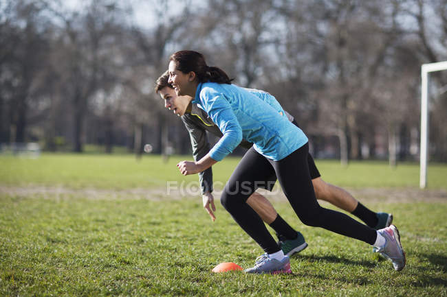 Young woman and man running from cone marker on playing field — Stock Photo