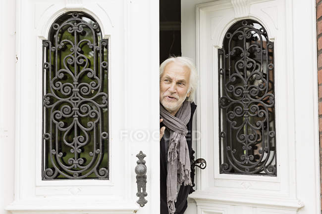 Homem sênior espreitando pela porta — Fotografia de Stock