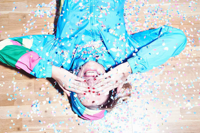 Estúdio tiro de jovem deitado no chão coberto de confete — Fotografia de Stock