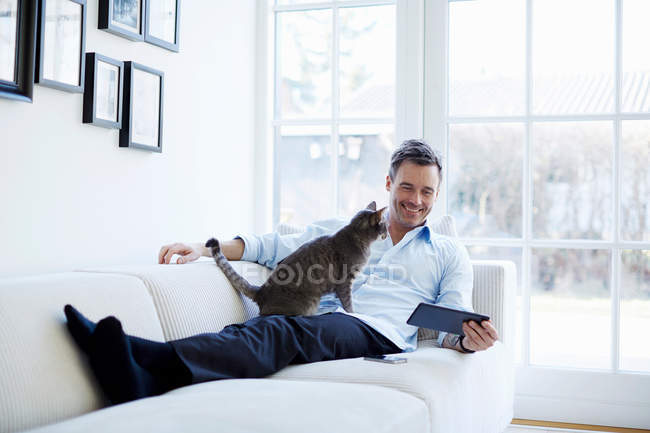 Homme relaxant sur canapé avec tablette numérique avec chat — Photo de stock