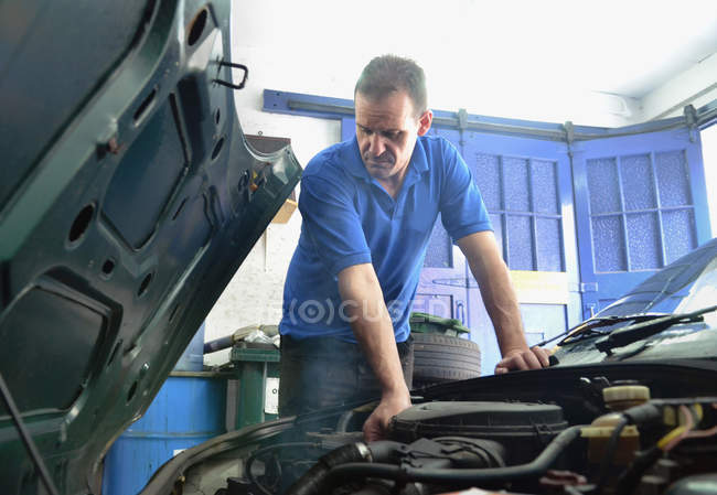 Mécanicien mâle vérifiant le moteur de voiture dans le garage — Photo de stock