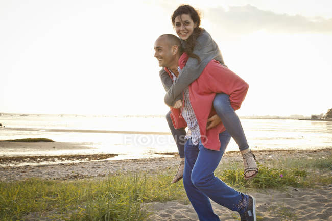 Hombre dando paseo a cuestas a la mujer en la playa - foto de stock