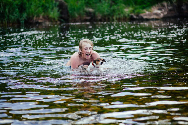 Молодий чоловік і його собака грають у річці — стокове фото