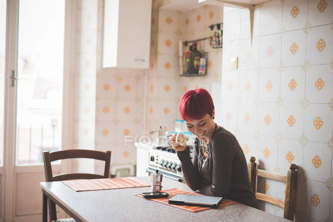 Junge Frau sitzt am Tisch und trinkt Kaffee, schaut auf digitales Tablet — Stockfoto