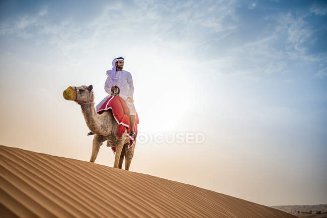 Homem vestindo roupas tradicionais do Oriente Médio montando camelo no deserto, Dubai, Emirados Árabes Unidos — Fotografia de Stock