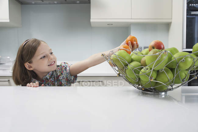 Elementary age girl reaching for tangerines from fruit bowl — Stock Photo