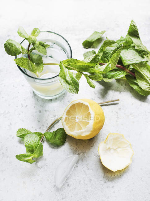 Glass with water, mint and lemon half on table — Stock Photo