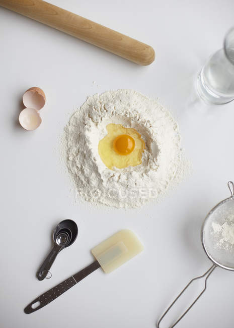 Top view with raw egg in center of flour stack and kitchen utensils — Stock Photo